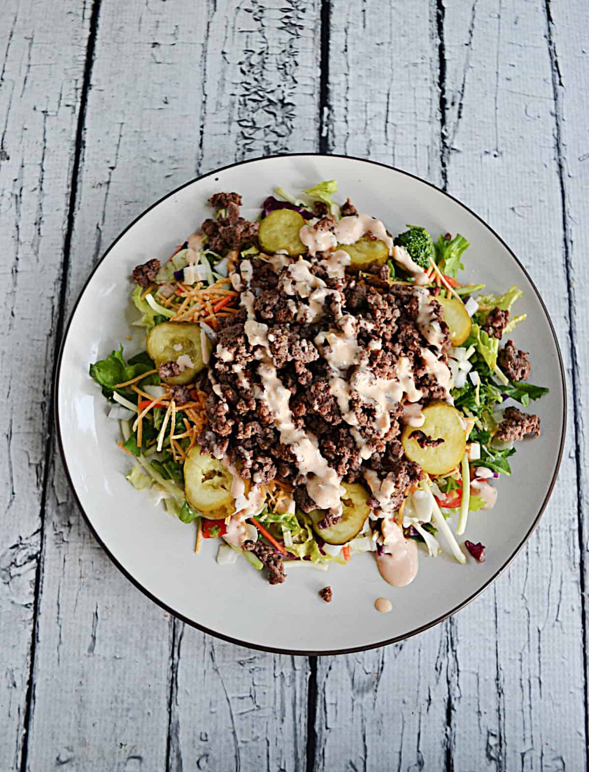 A plate of salad with pickles and beef on top.