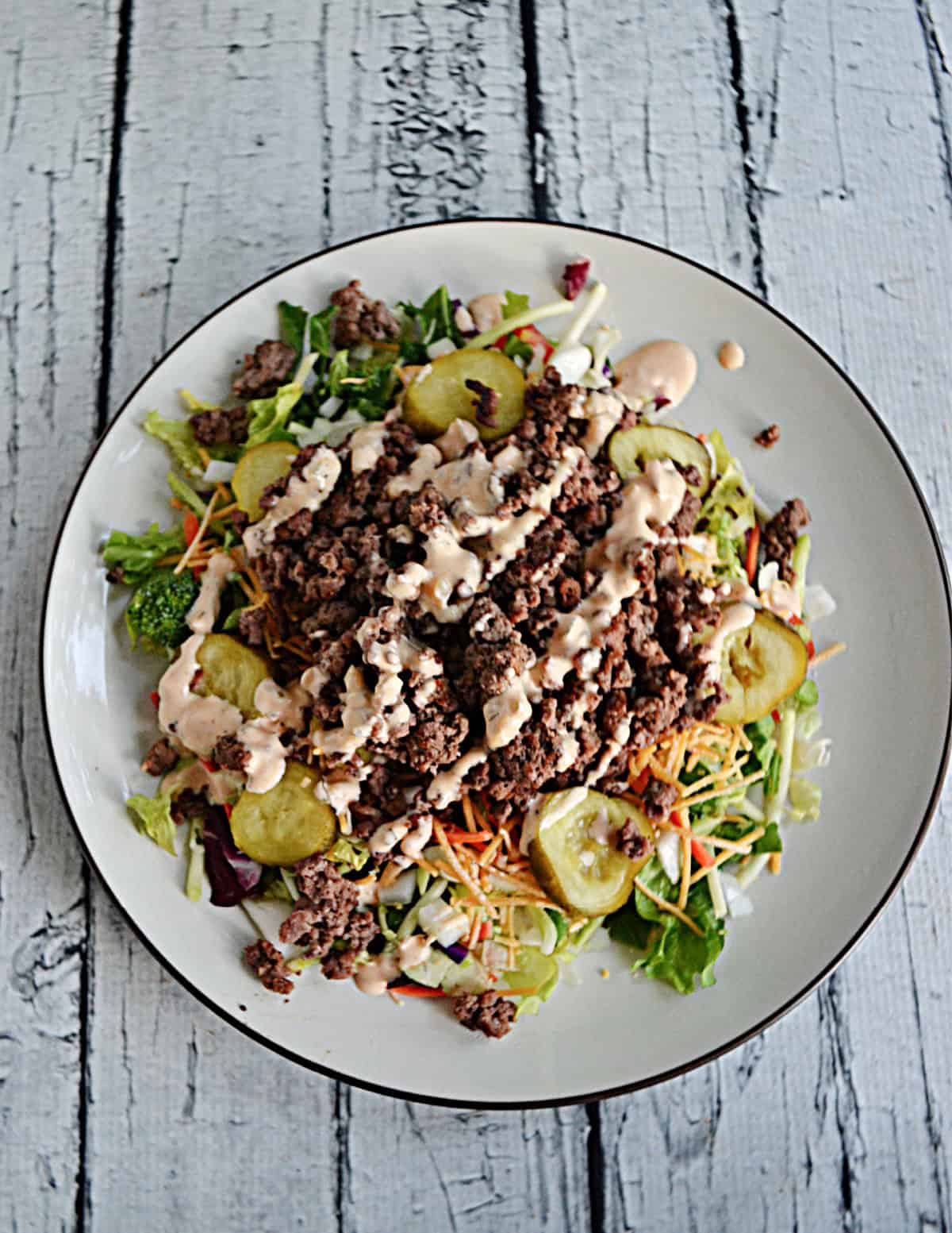 A salad with beef, pickles, cheese, and sauce on top.