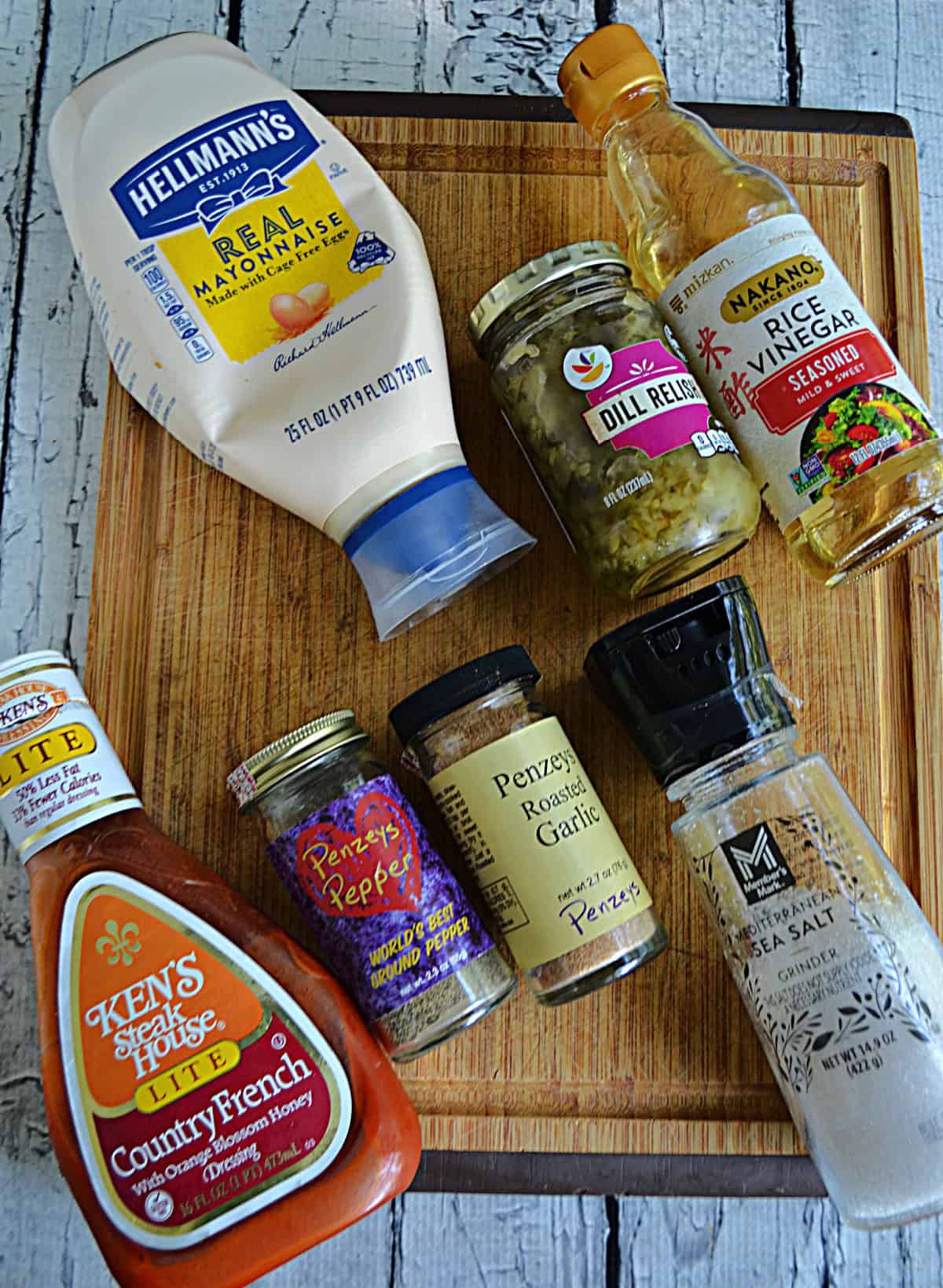 A cutting board with mayonaaise, pickle relish, vinegar, spices, and salt on it.