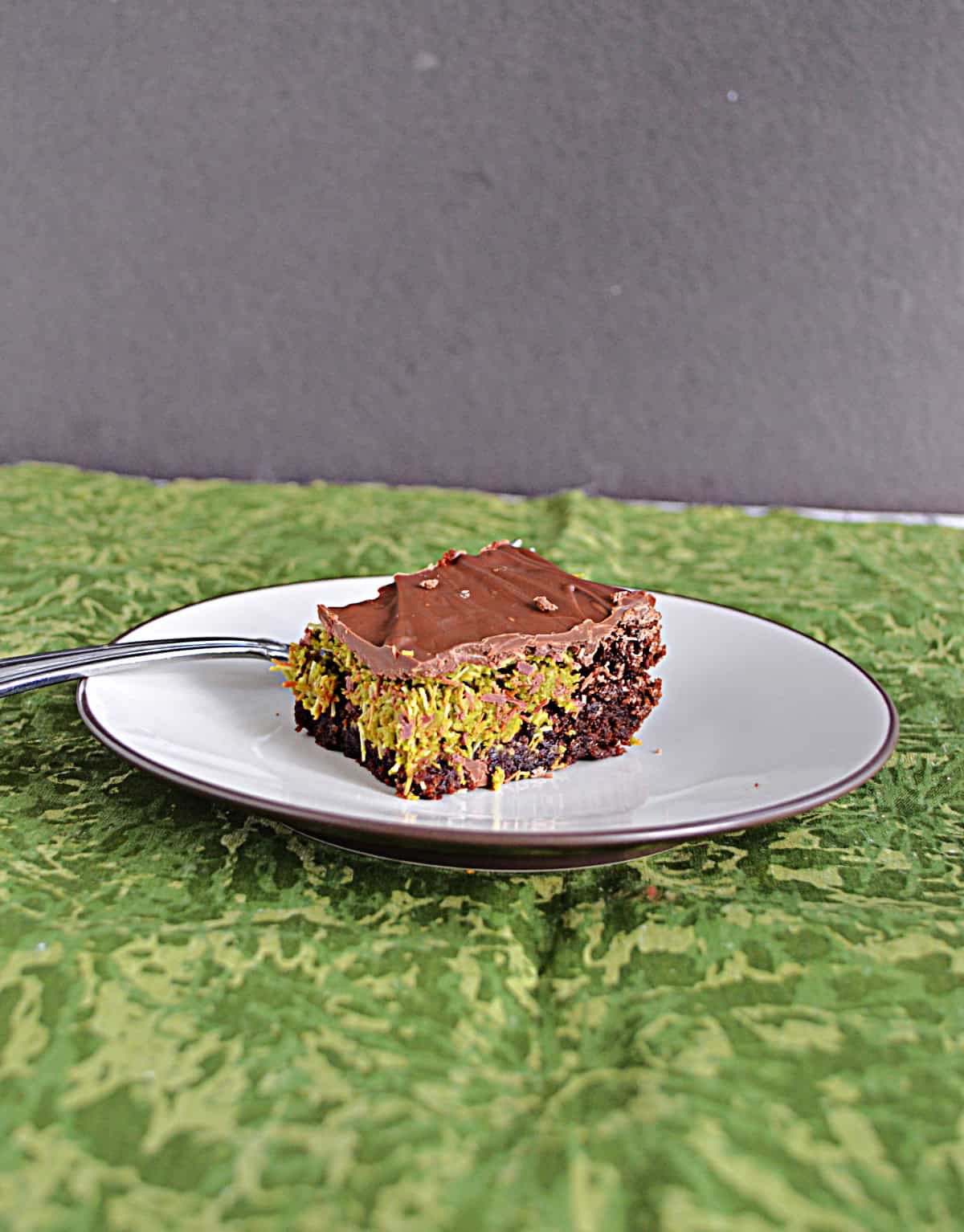A side view of a brownie with a pistachio layer and a chocolate layer on top.