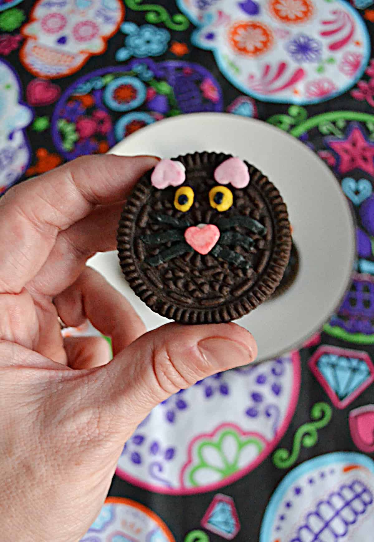 A hand holding a black cat cookie.