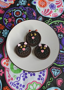 Three black cat face cookies on a plate.