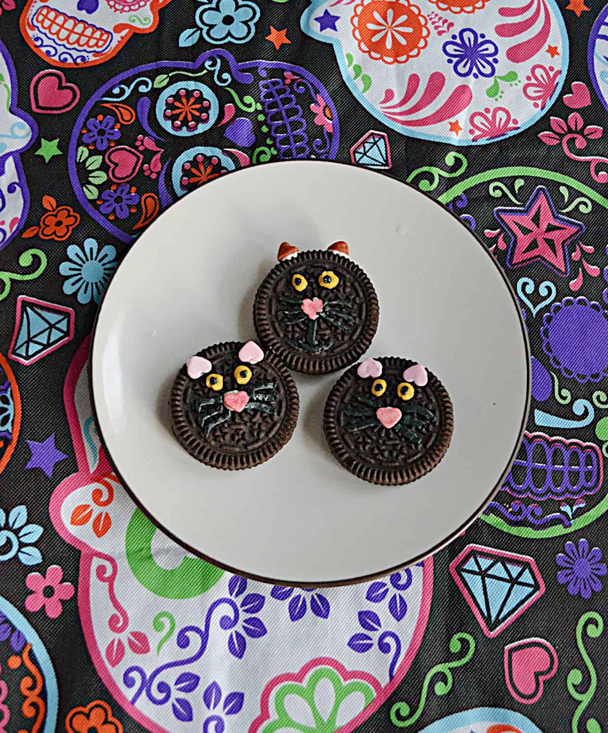 Three black cat face cookies on a plate.
