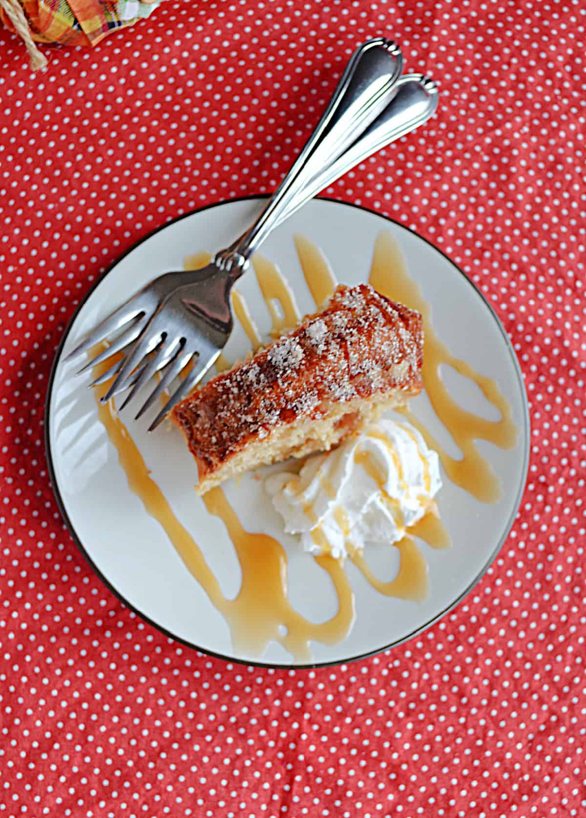 A plate with a slice of cake, a caramel drizzle, whipped cream, and two forks on it.