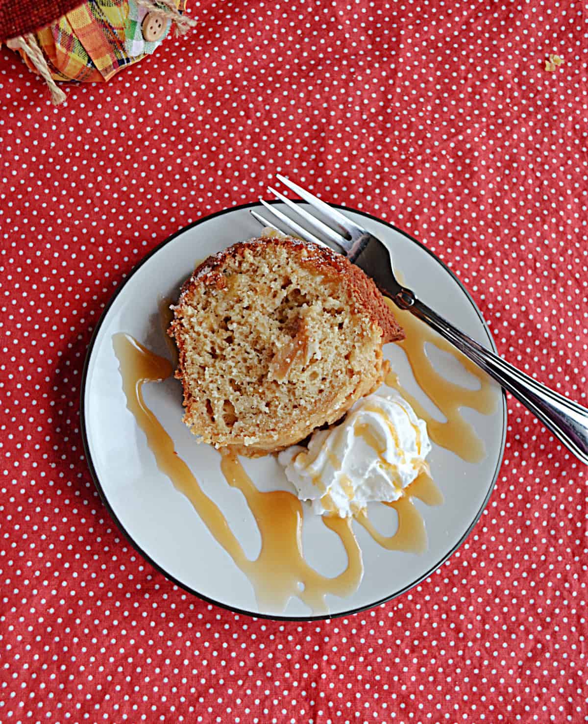 An overhead view of a slice of cake with a caramel drizzle, whipped cream, and a fork on the plate.