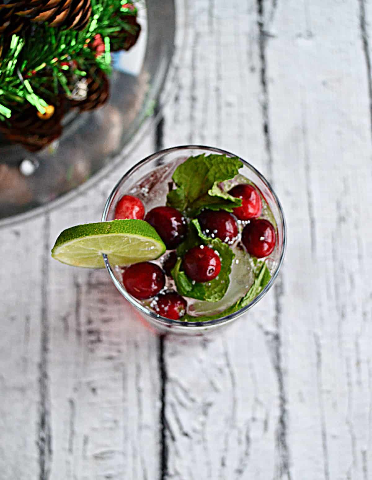 A top view of a glass with cranberries mint leave, and a lime wedge on top.