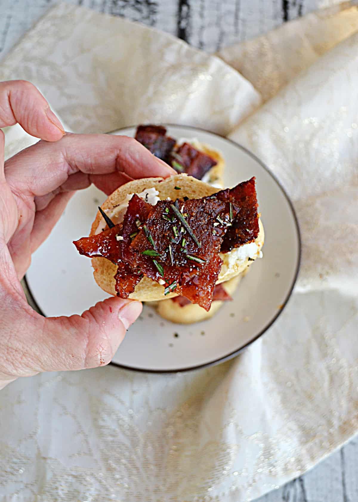 A hand holding a crostini with bacon on it.