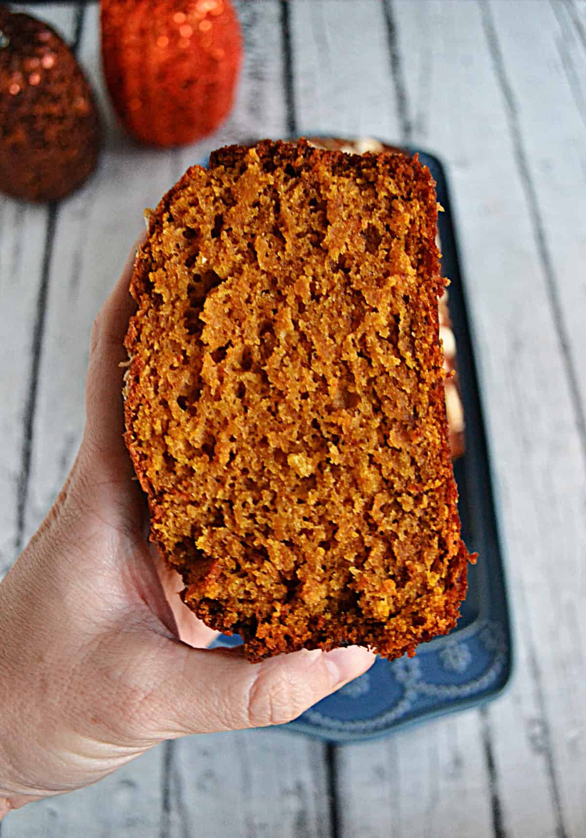 A hand holding a slice of pumpkin bread.
