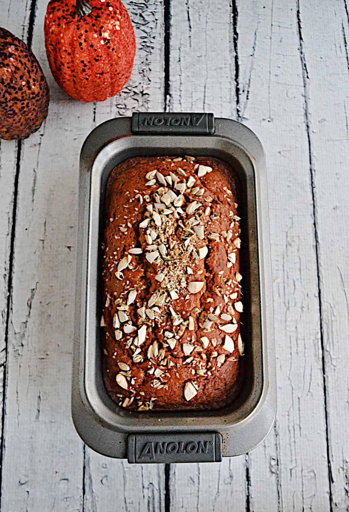 A pan of baked pumpkin bread with two pumpkins in the background.