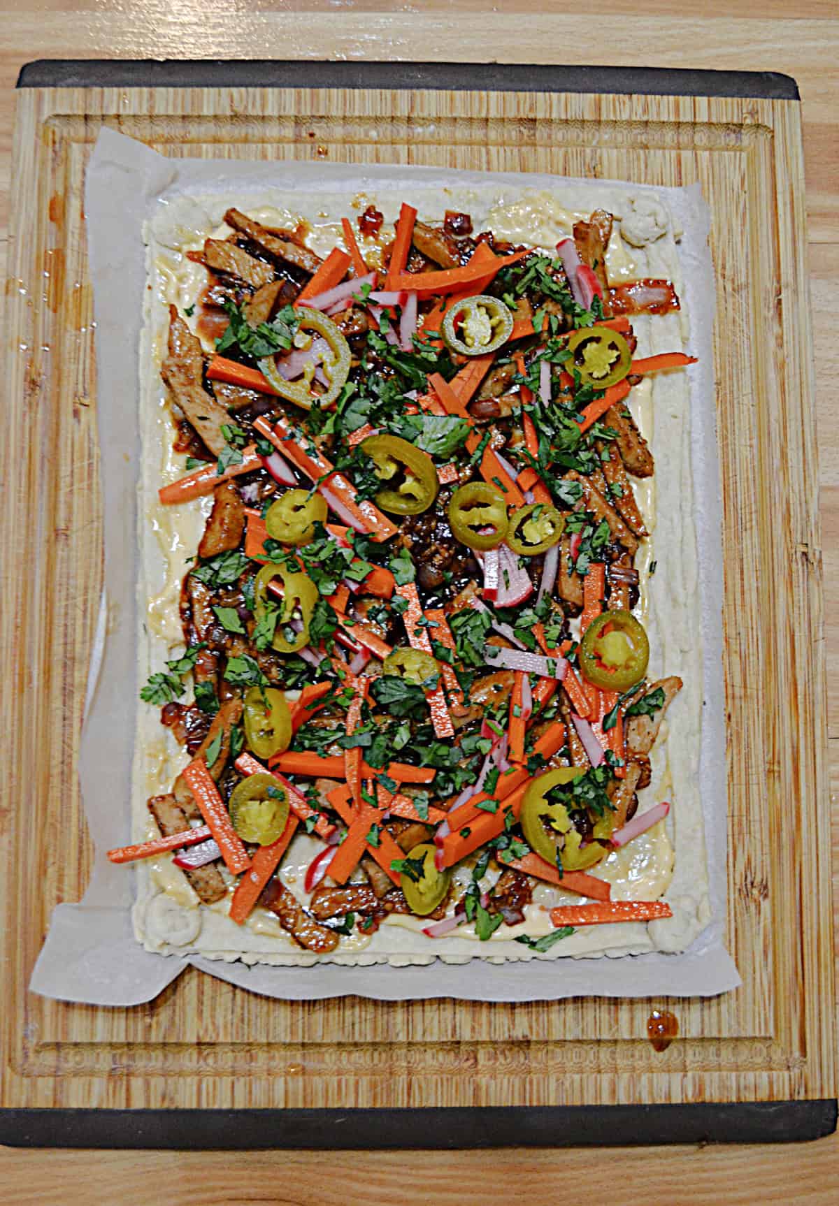 A tart shell with vegetables and pork on it.