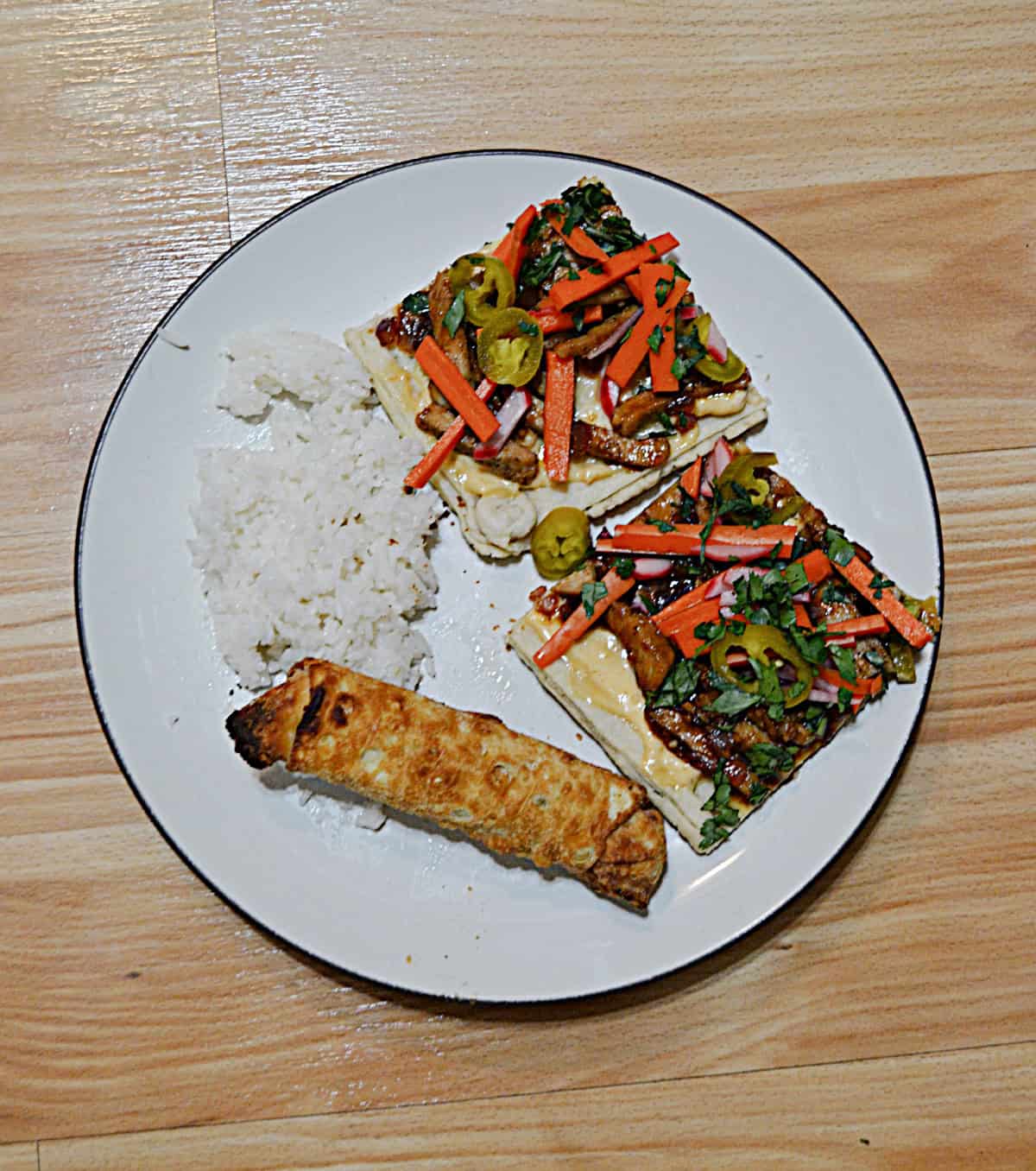 A plate with rice, an egg roll, and two slices of tart with pork and vegetables.