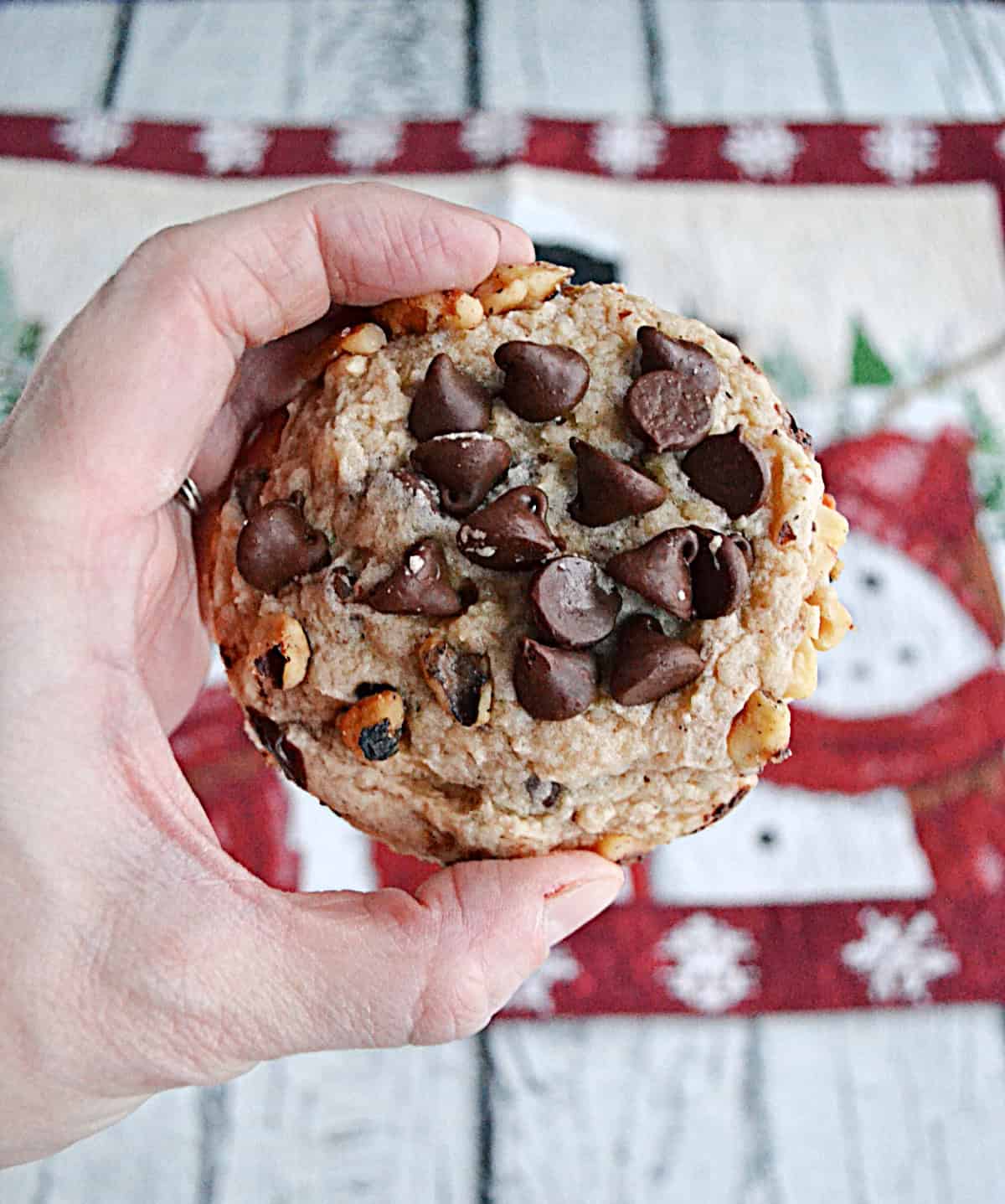 A hand holding a cookie with chocolate chips on top of it.