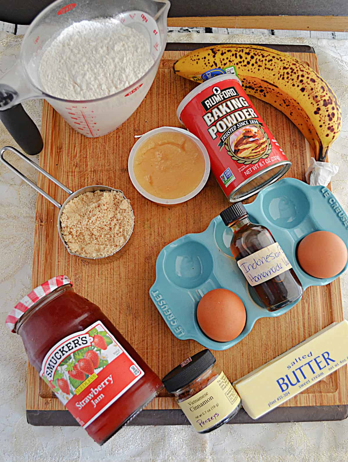A cutting board with strawberry jam, sugar, butter, flour, a banana, and spices on it.