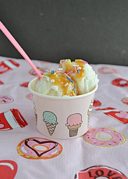 A cup with 2 scoops of ice cream covered in caramel and a spoon.