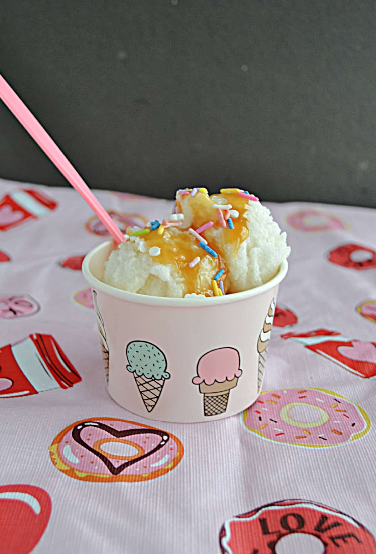 A cup with 2 scoops of ice cream covered in caramel and a spoon.