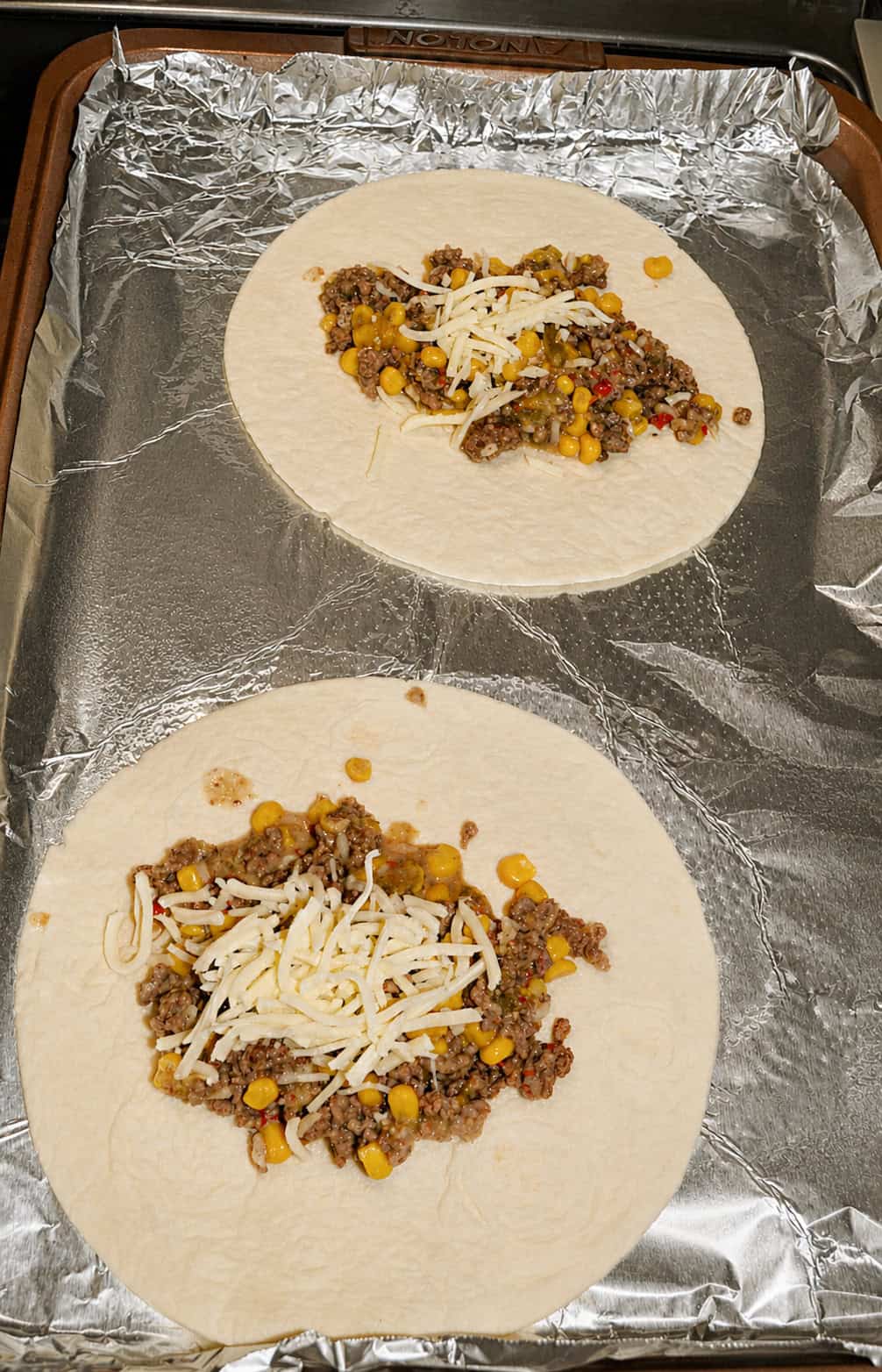 A sheet pan with two tortillas topped with beef, corn, and cheese.