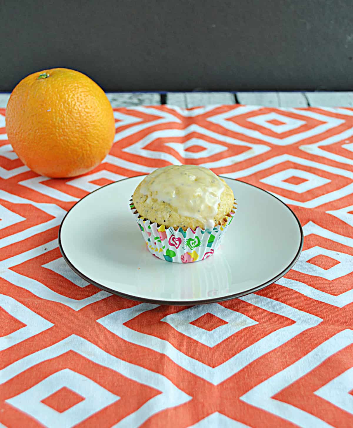 A muffin on a plate with an orange behind it.