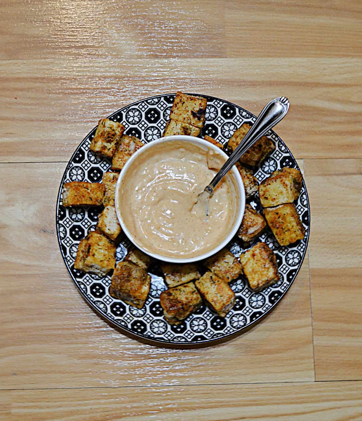 A plate with tofu bites on it and a sauce in the middle.