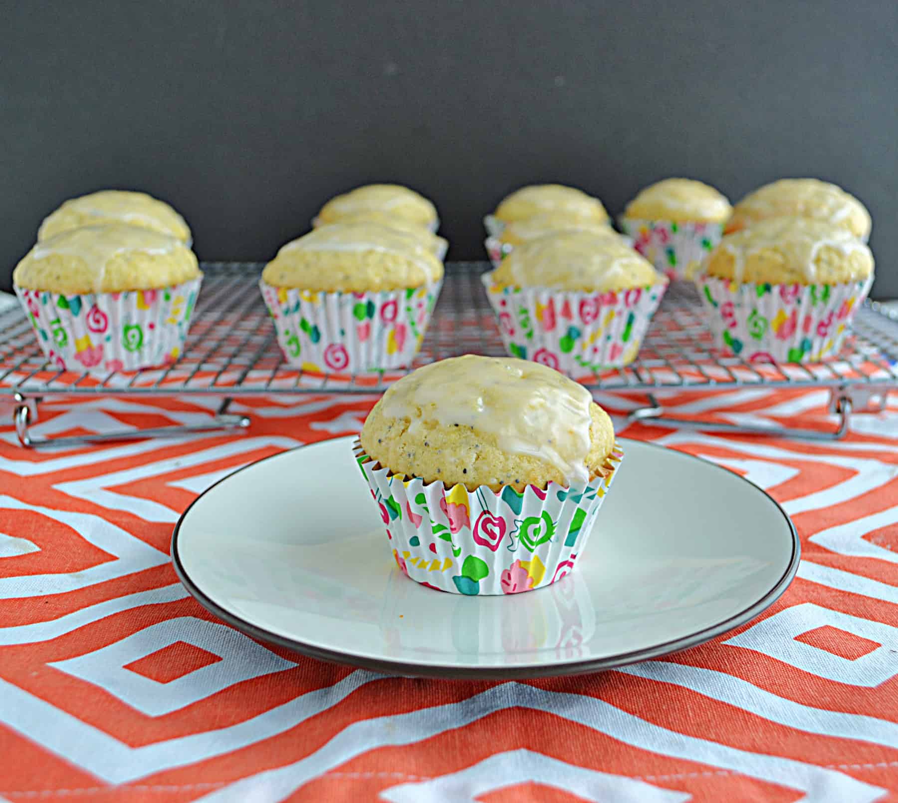 A muffin on a plate with a dozen muffins behind it.
