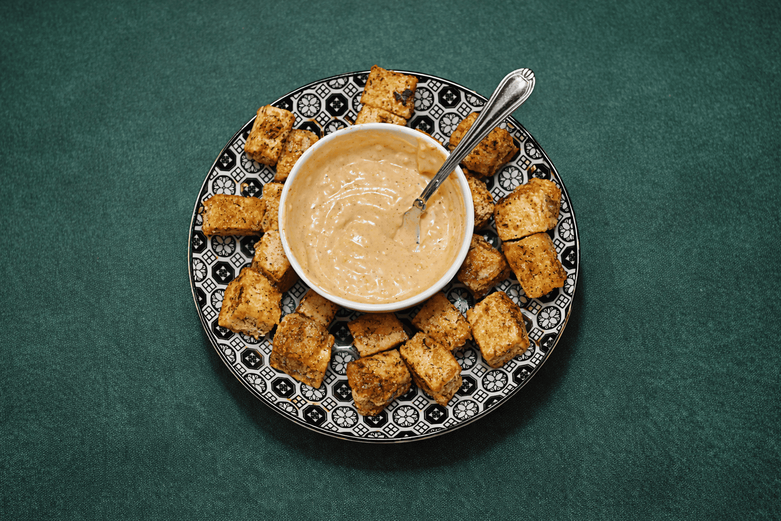 A plate of tofu bites with a bowl of sauce in the middle.