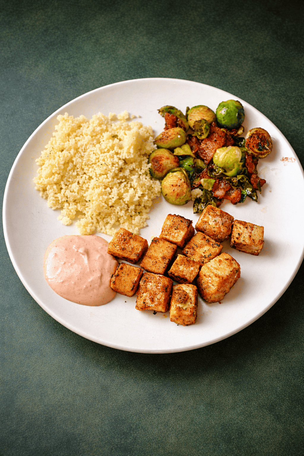 A plate with tofu bites, sauce, couscous, and Brussels sprouts.
