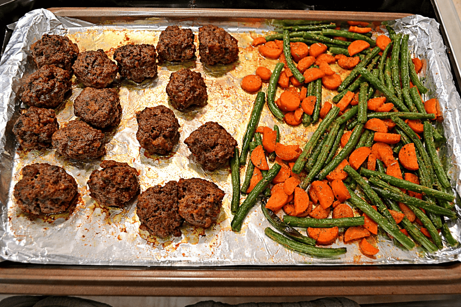 A sheet pan with meatballs on one side, carrots and green beans on the other.