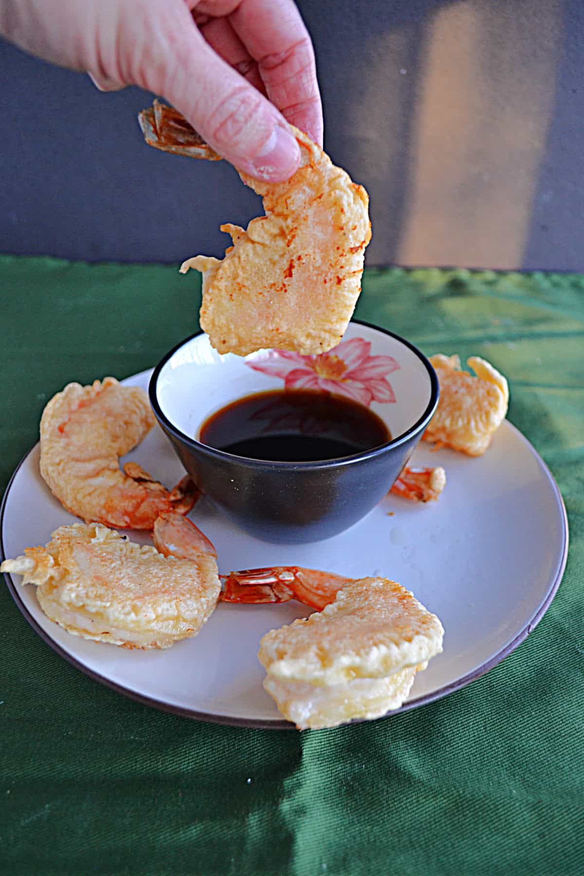 A hand holding a golden brown shrimp over top of a bowl of dipping sauce.