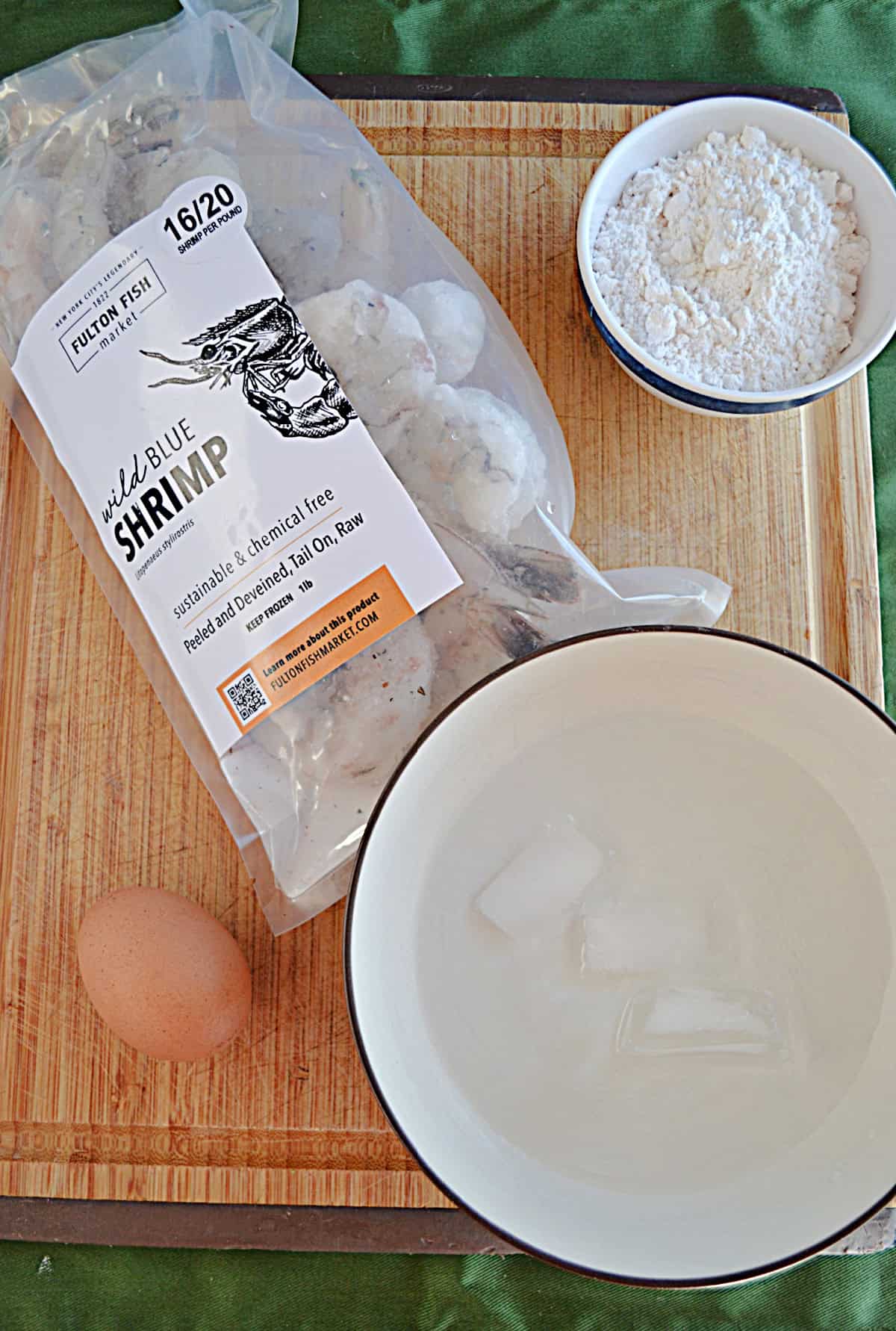 A bag of shrimp, a bowl of flour, an egg, and ice water.