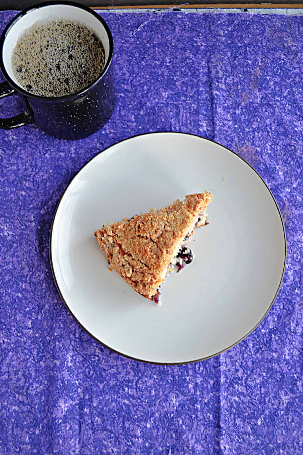 A plate with a slice of coffee cake and a mug of coffee behind the plate.