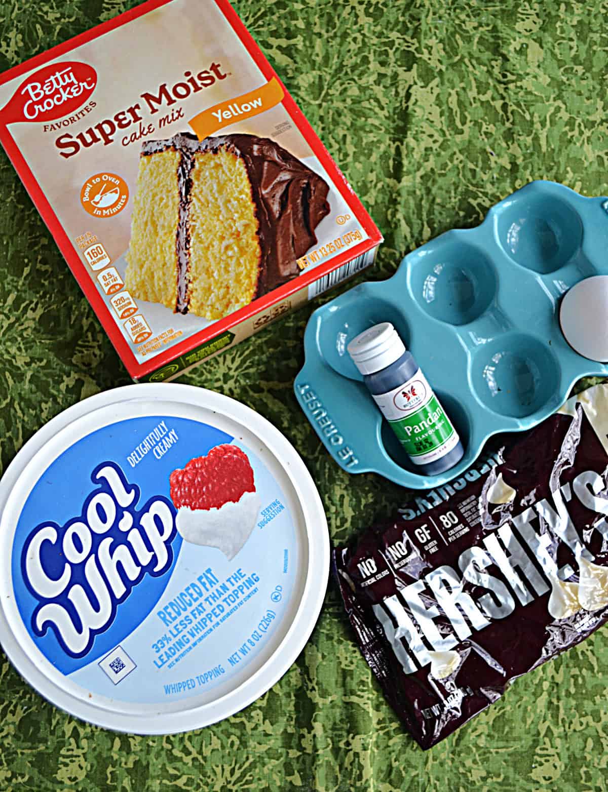 A box of cake mix, a container of Cool Whip, a bag of white chocolate chips, and pandan extract.