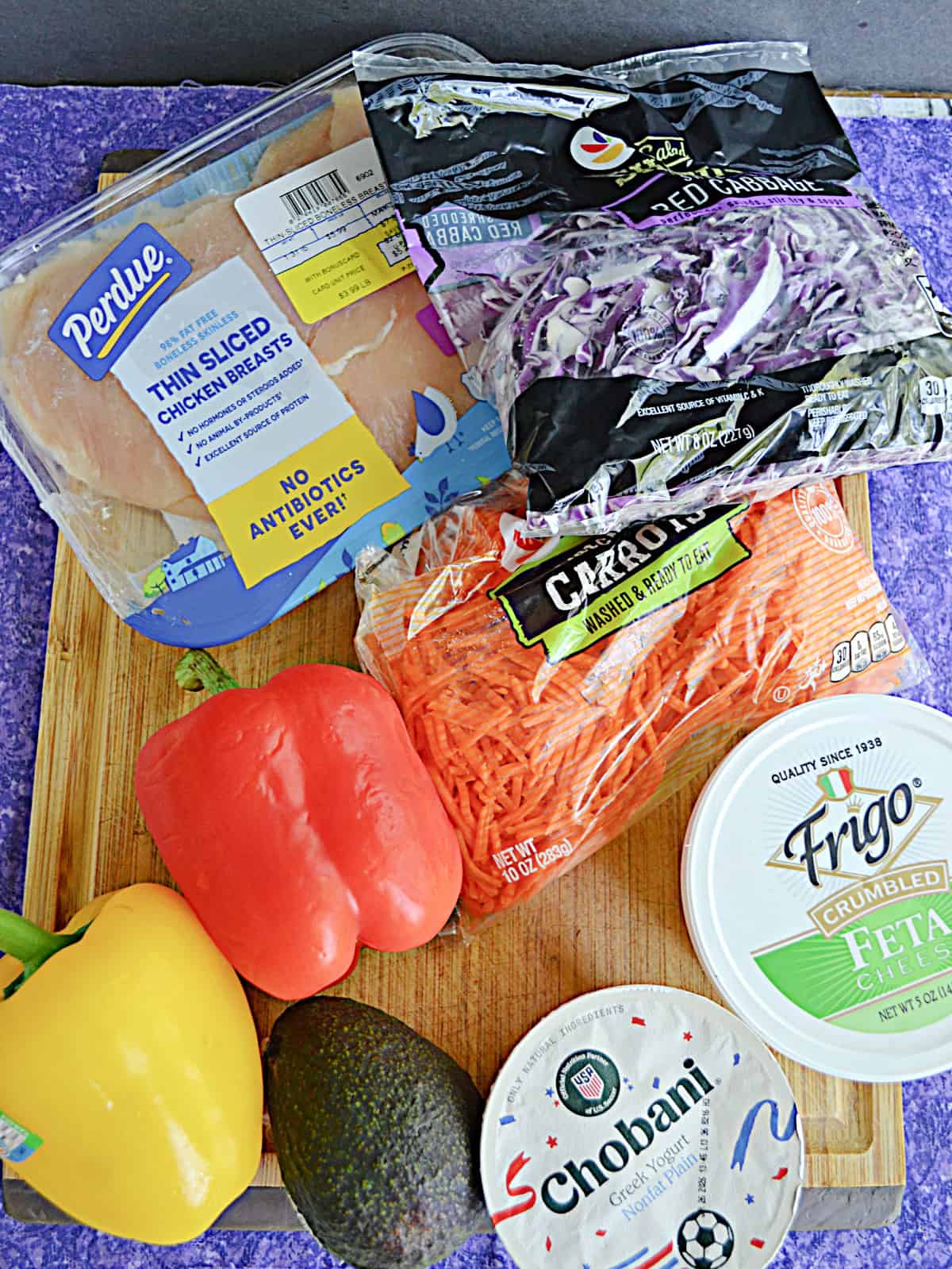 A cutting board with chicken, peppers, feta cheese, cabbage, yogurt, and an avocado on it.
