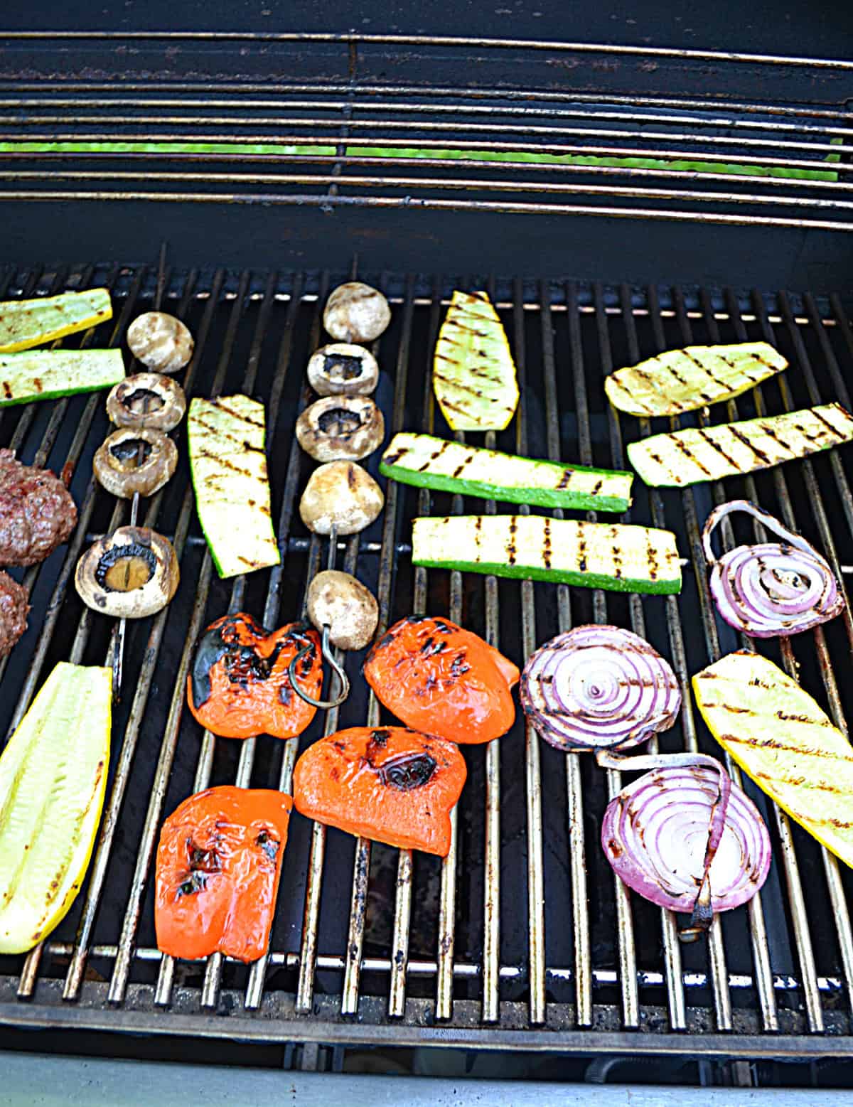 A grill with zucchini, peppers, red onions, and mushroom skewers on it.
