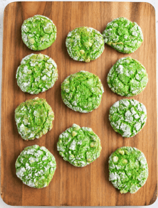 A cutting board with green cookies on it.