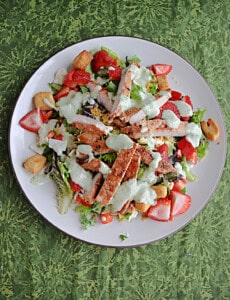 Plate of salad with pork, strawberries, and garden ranch on top.