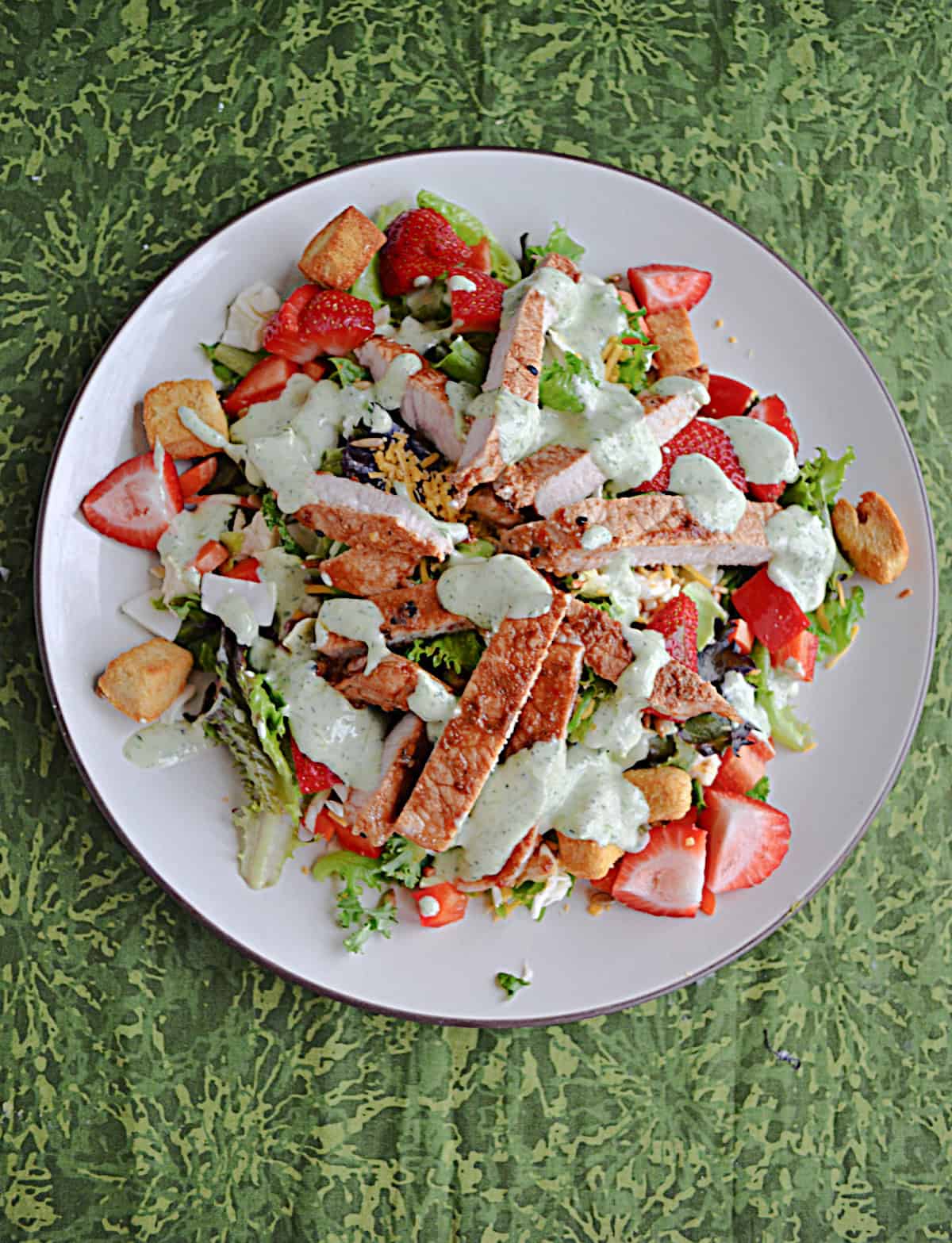 Plate of salad with pork, strawberries, and garden ranch on top.