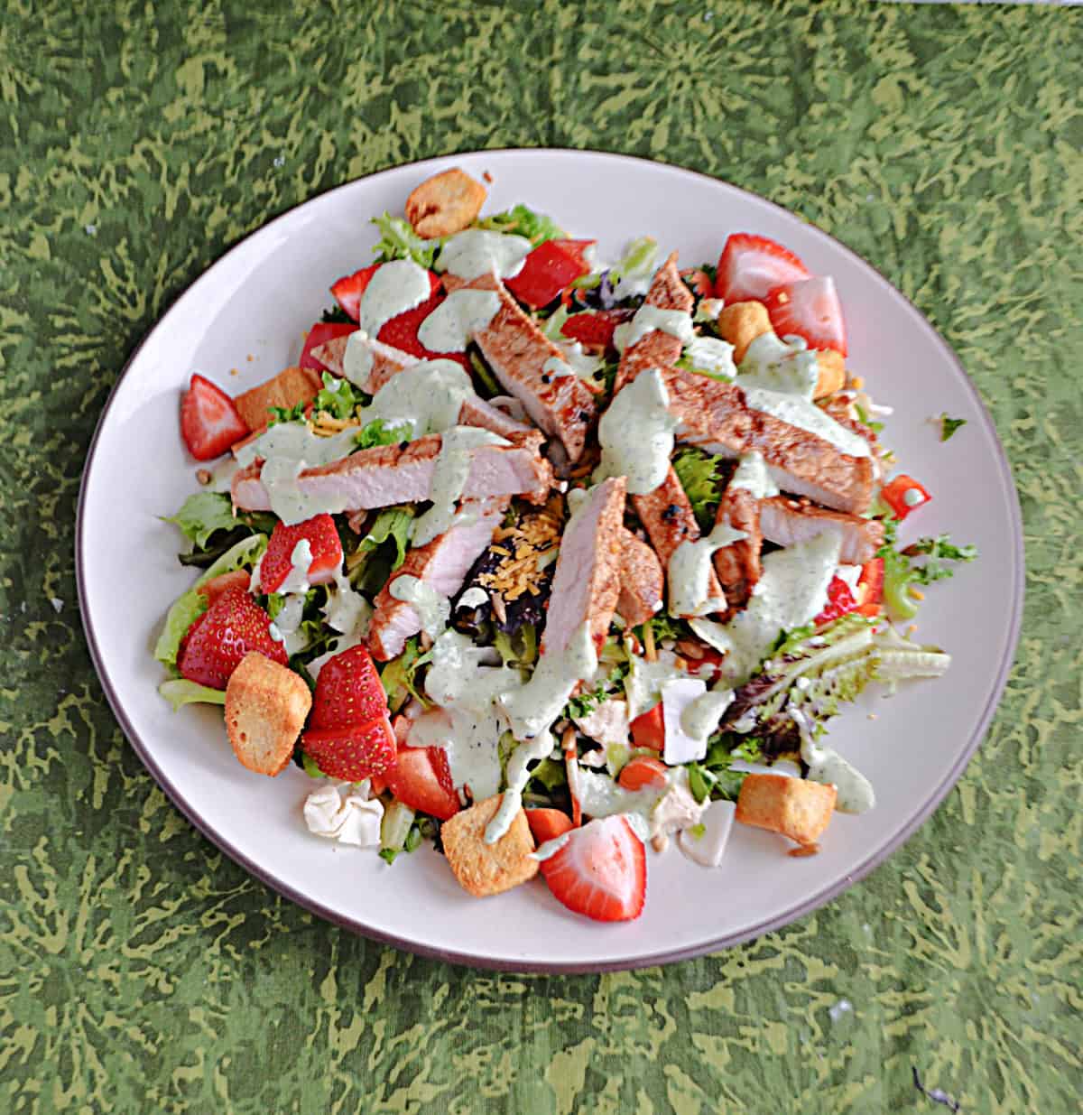 A plate of salad with pork, ranch, and strawberries on top.