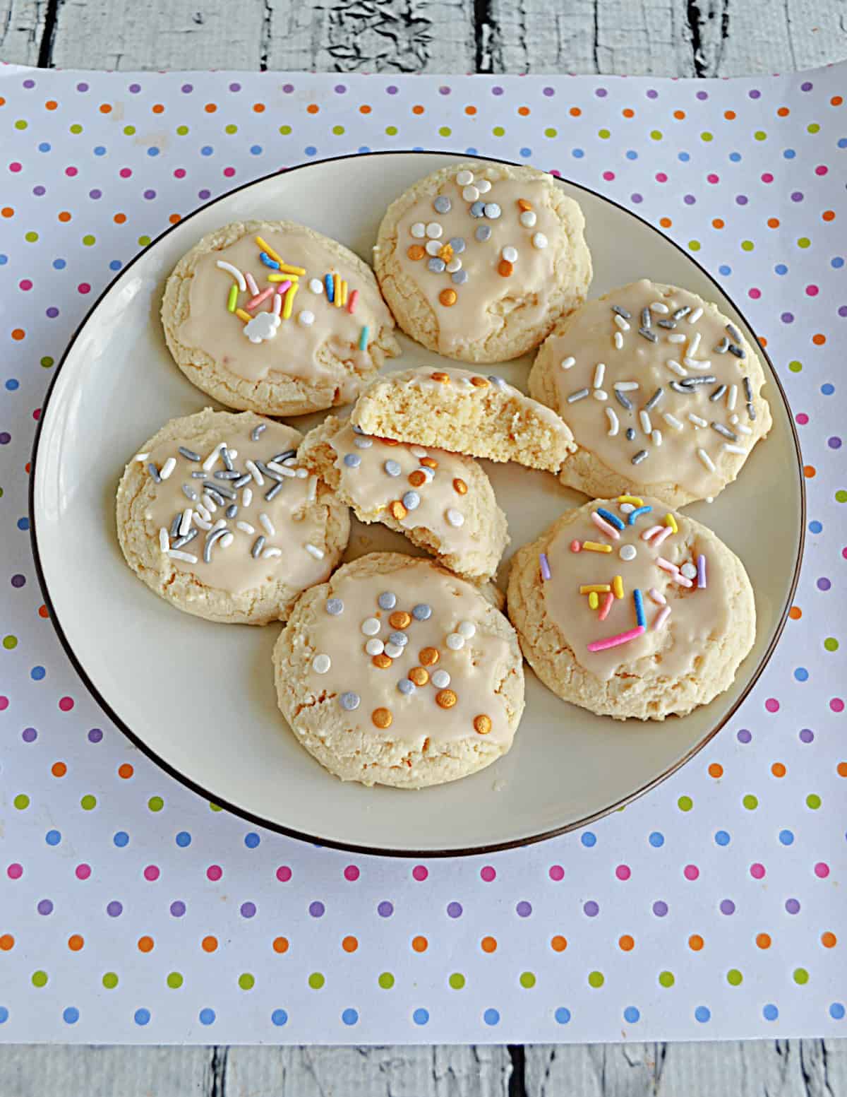A plate of sugar cookies that are glazed with sprinkles on top with the center cookie being broken in half.