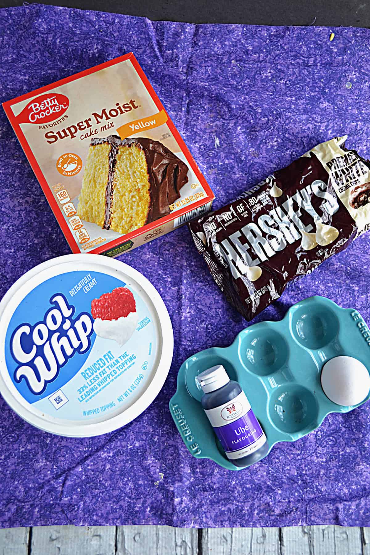 A box of cake mix, a bag of white chocolate chips, an egg, a container of Cool Whip, and ube extract.