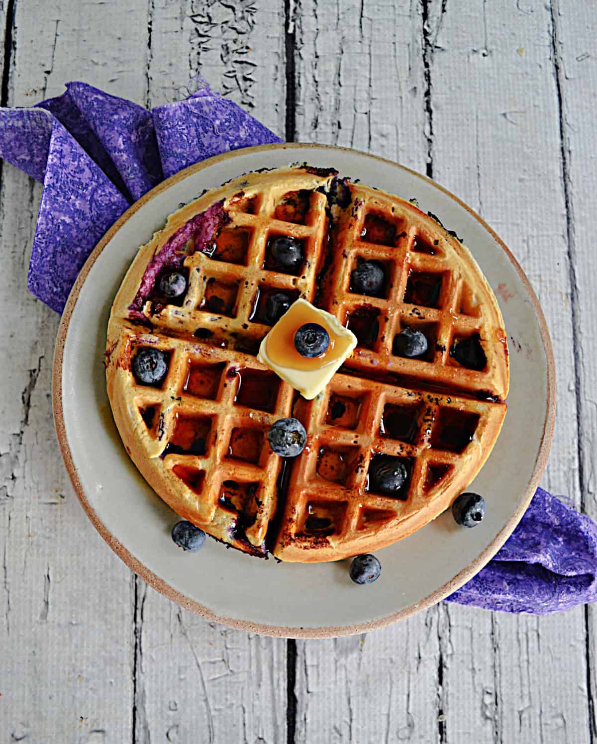 A waffle with fresh blueberries, butter, and syrup on it.