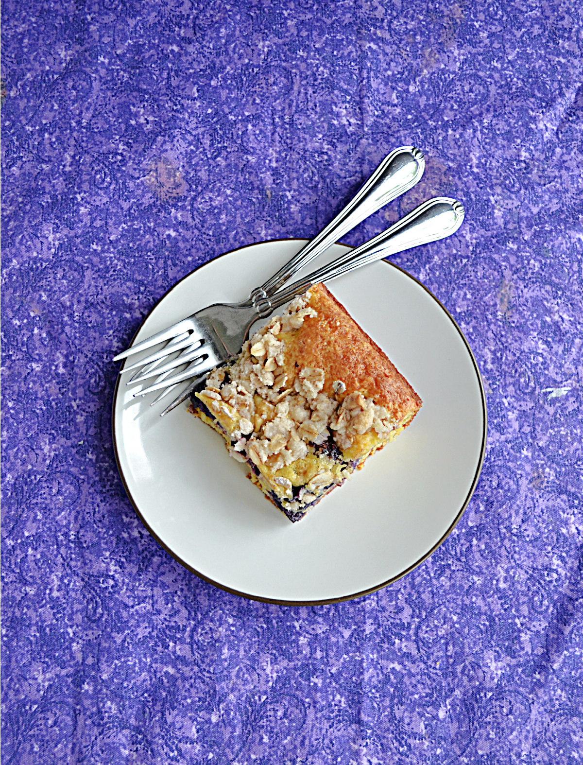 A plate with a piece of coffee cake and 2 forks on it.