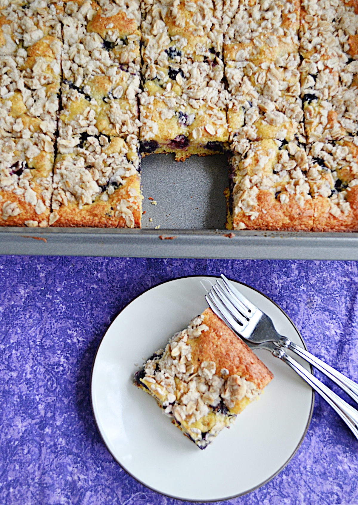 A pan of coffee cake with a piece missing and on a plate with two forks.