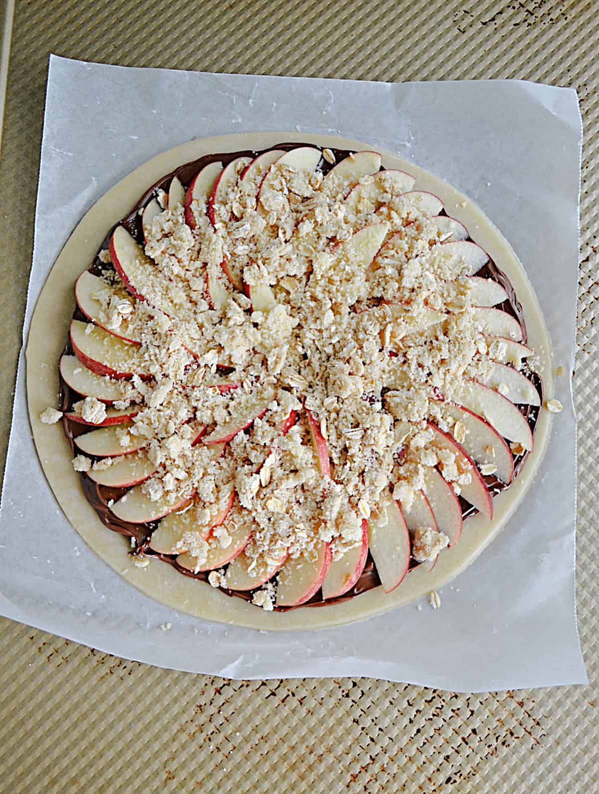 A pie crust topped with thinly sliced apples and a crumble.