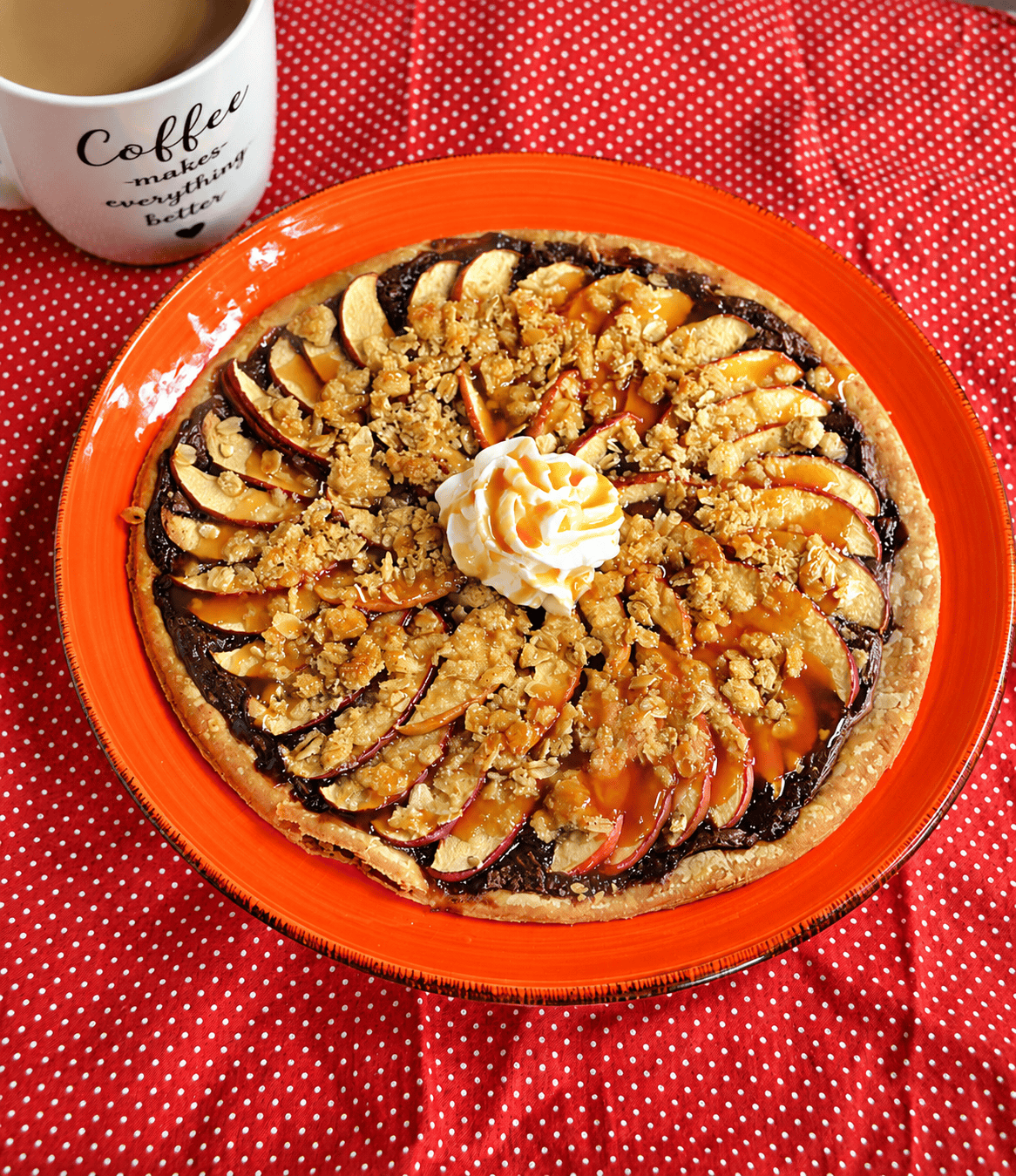 A plate with a dessert pizza with thinly sliced apples, a crumble, whipped cream, and a caramel drizzle and a cup of coffee.