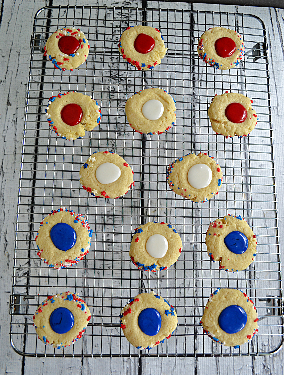 A wire rack with thumbprint cookies on it filled with red, white, or blue icing.