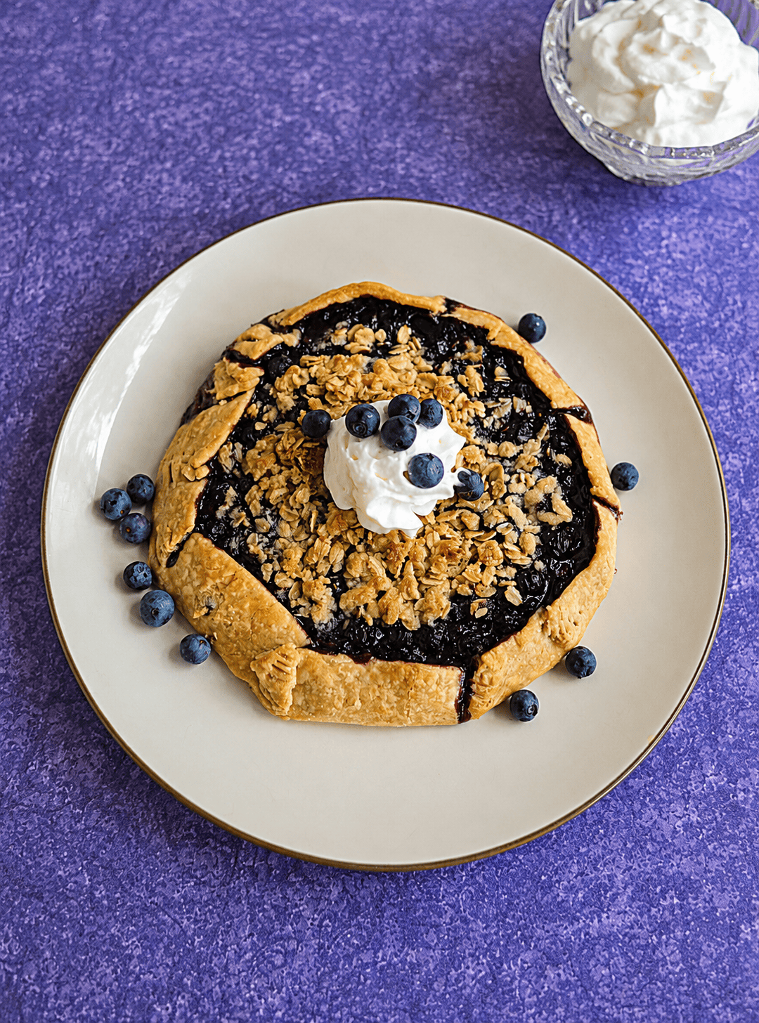 A blueberry galette with a dollop of whipped cream and fresh berries on top.