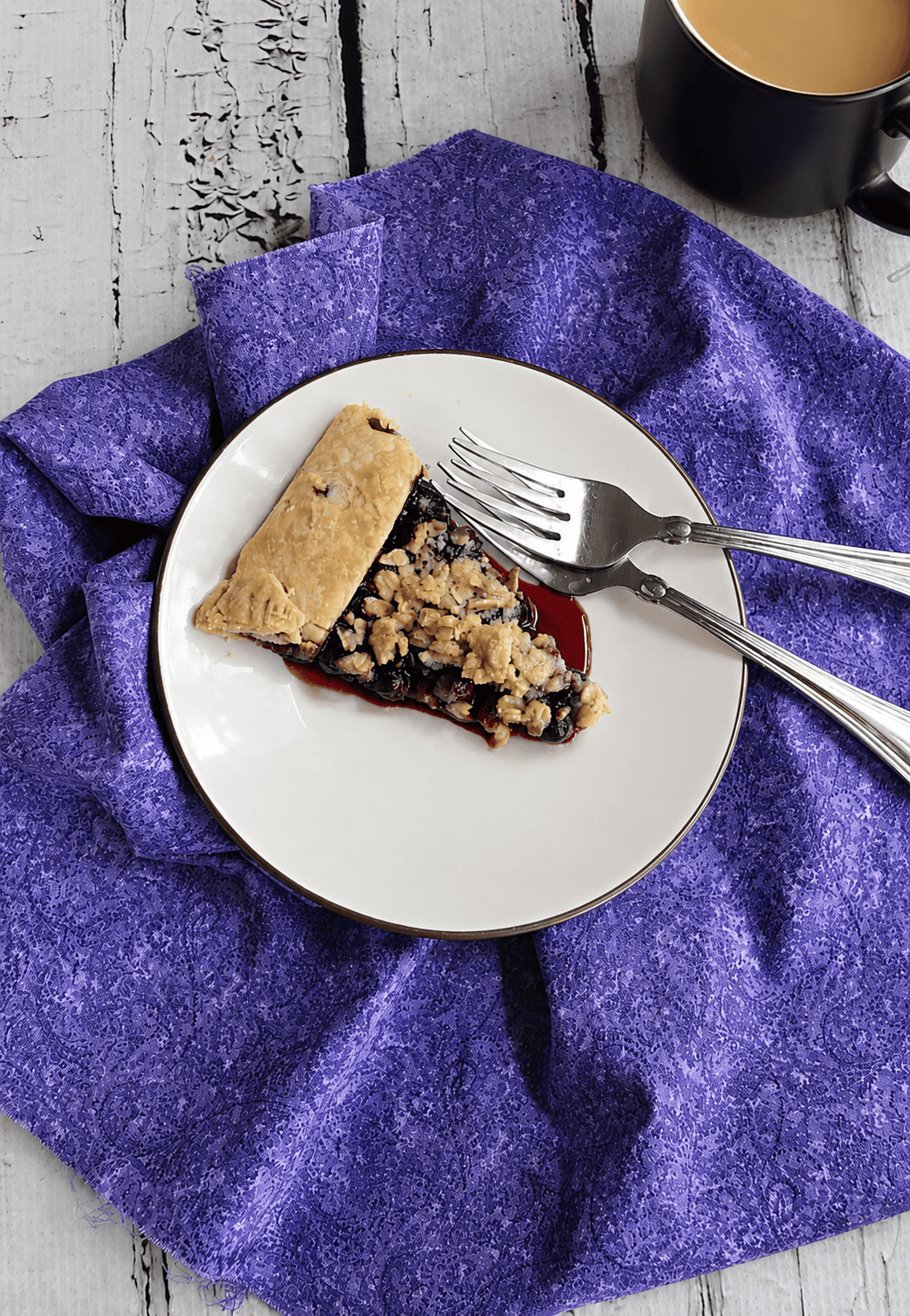 A plate with a slice of blueberry pie on it and 2 forks.