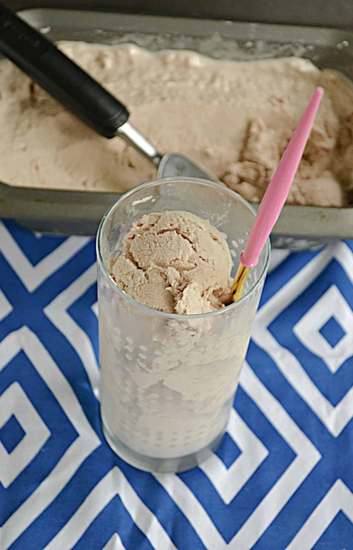A glass with chocolate Frosty in it along with a spoon and a pan of the Frozen Chocolate treat behind the glass .