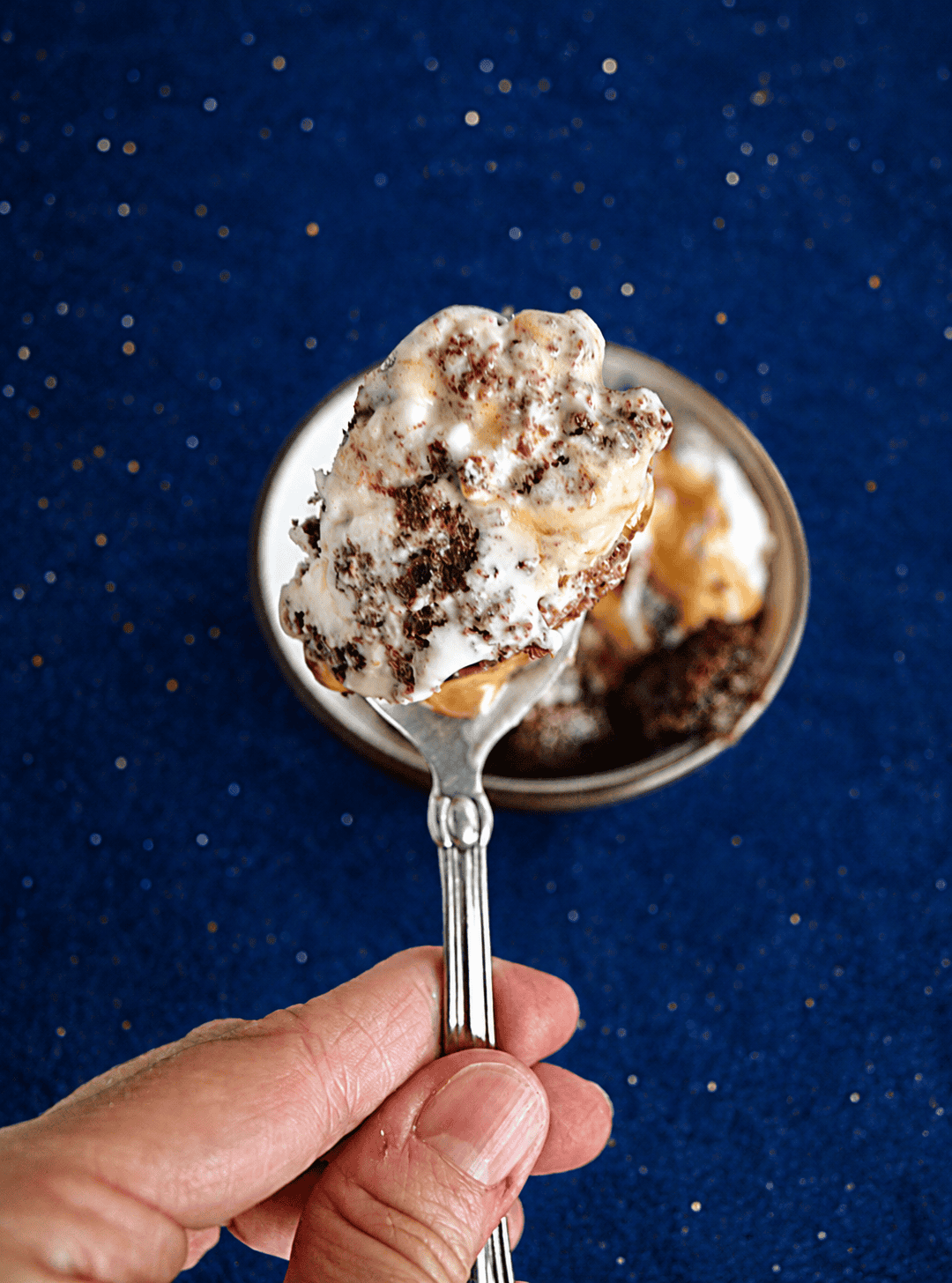 A hand holding a spoon with caramel brownie ice cream on it.