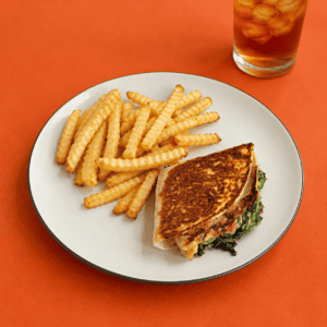A plate with a golden brown wrap on it along with fries and a glass of tea behind the glass.