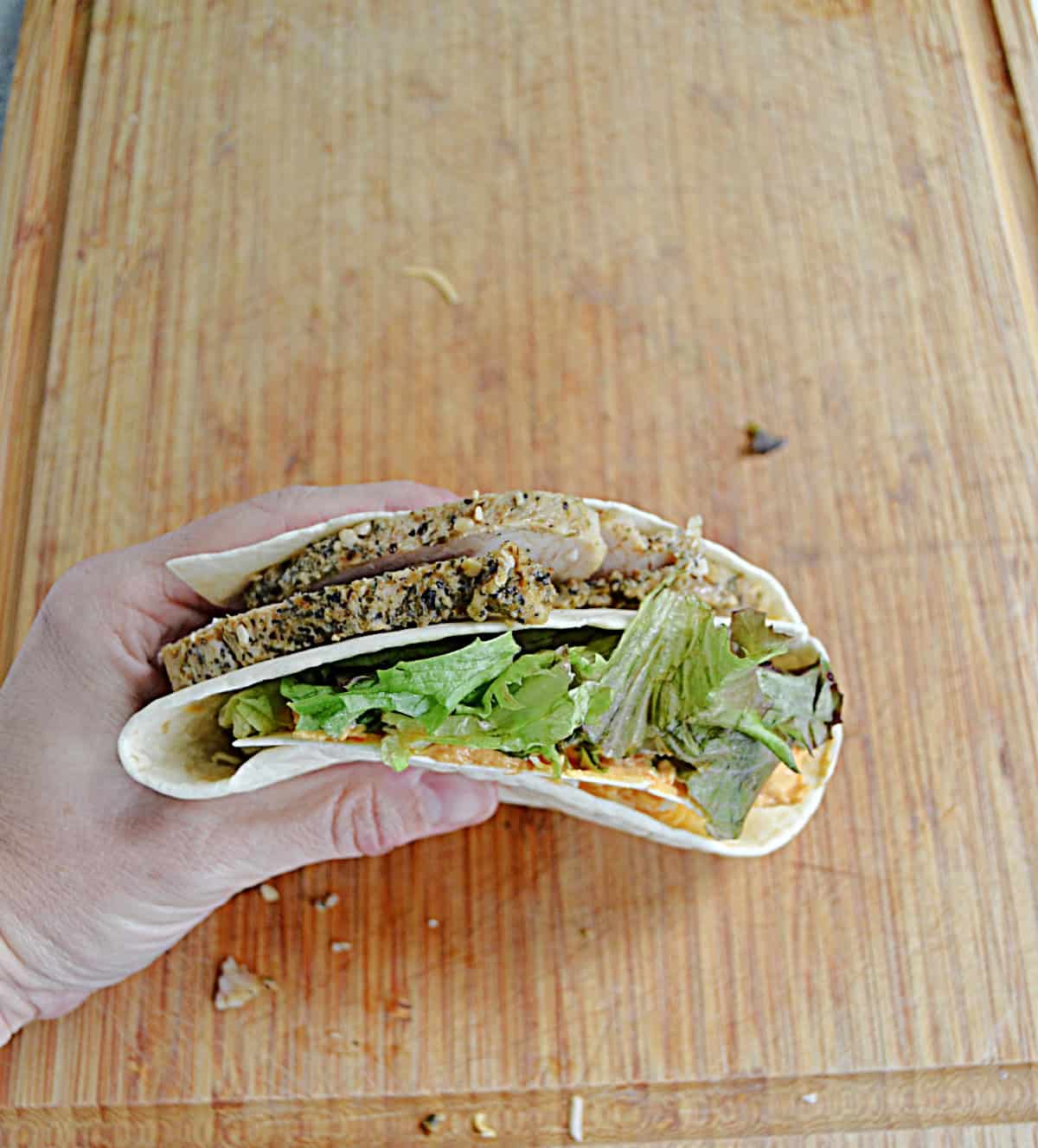 A hand holding a wrap with turkey, cheese, and vegetables in it soon.